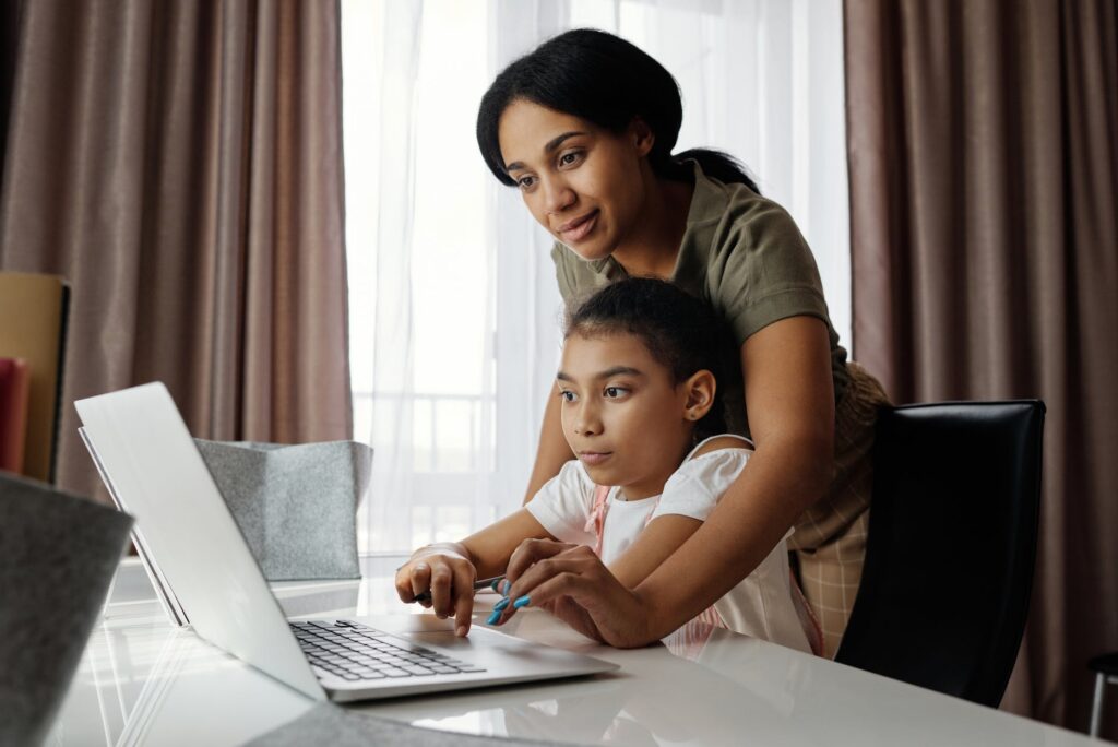 mother helping her daughter use a laptop